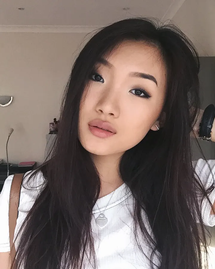 Jeune femme asiatique en t-shirt blanc, tenant ses cheveux noirs, regardant l'appareil photo