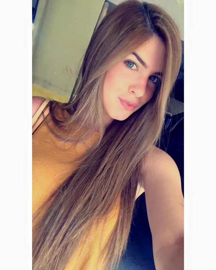 Jeune femme aux longs cheveux bruns et yeux bleus, portant un haut jaune, regardant vers l'appareil photo.