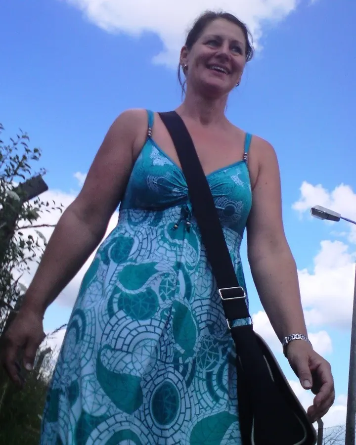 Femme aux cheveux châtains, en robe colorée, assise sur une chaise blanche sur un balcon avec vue sur des palmiers.