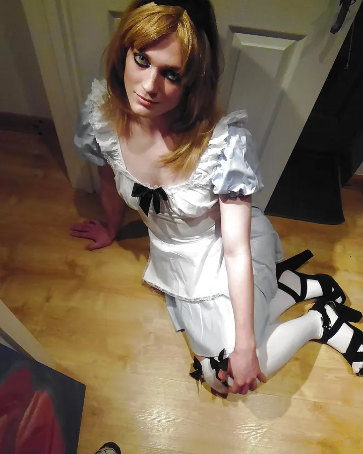 Femme blonde aux cheveux roux, souriante, robe noire, collants résille, talons hauts, assise sur bureau, tablette en main.