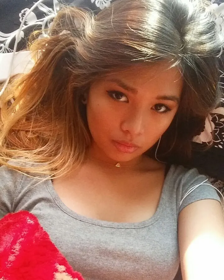 Femme aux cheveux foncés portant un haut gris, allongée sur un lit avec un plaid rouge.