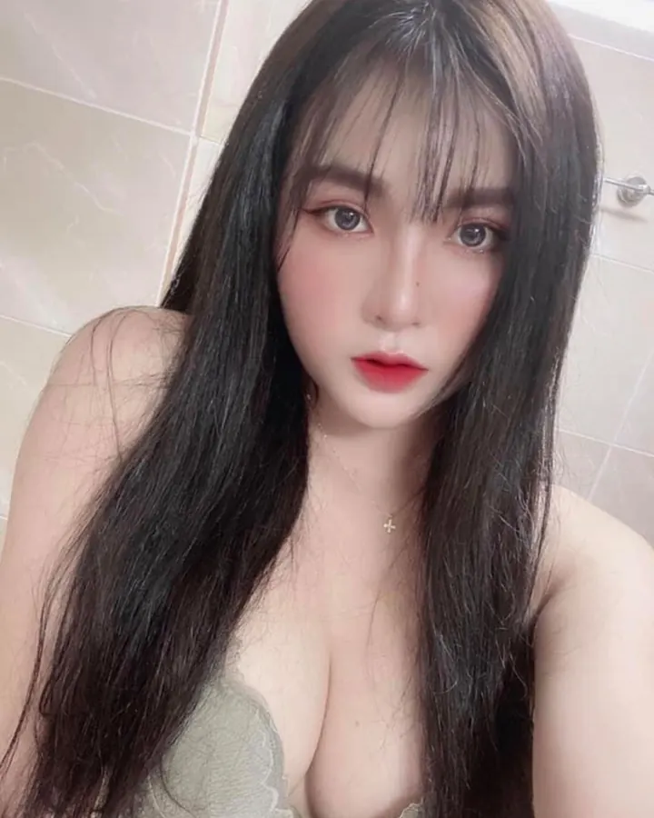 Femme aux cheveux foncés portant un haut gris, allongée sur un lit avec un plaid rouge.