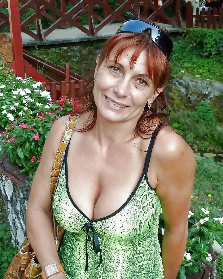 Femme aux cheveux roux en robe verte à imprimé serpent, souriante, en extérieur verdoyant.