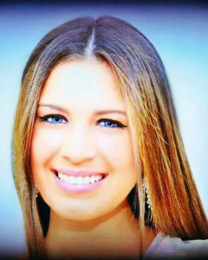 Femme blonde aux yeux bleus souriante, cheveux longs, sur fond clair.