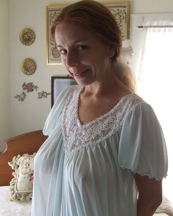 Femme blonde en robe noire, posant sur un canapé beige, bas noirs, talons hauts.
