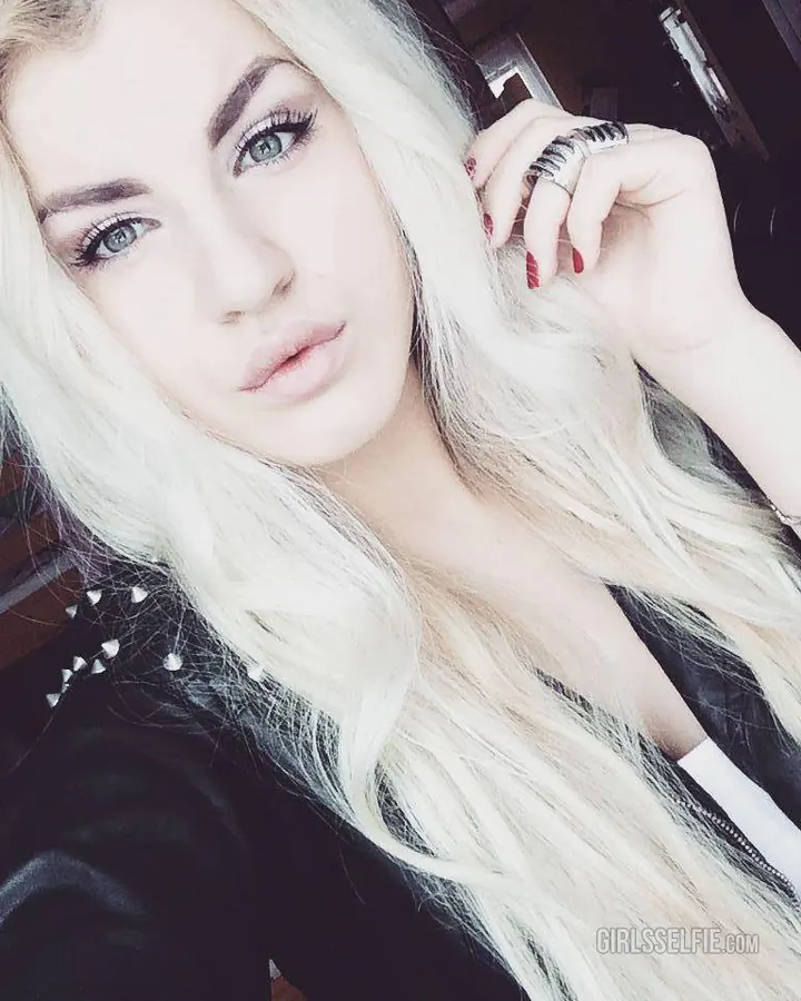 Jeune femme aux cheveux blonds et yeux bleus, regardant directement l’objectif, coiffure légèrement décoiffée, sourire discret.