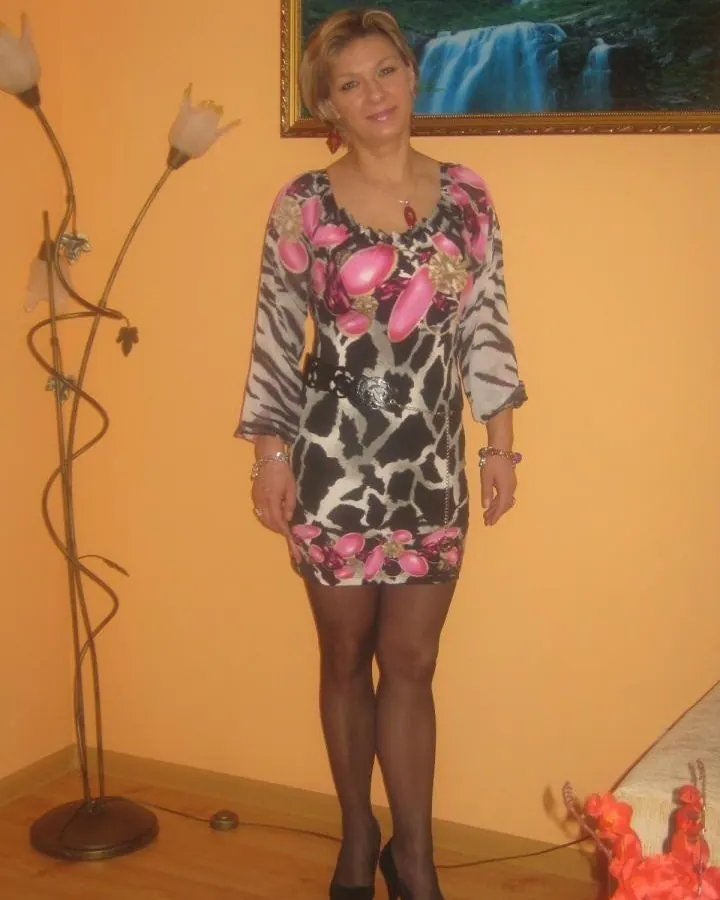 Femme en robe imprimée zèbre et fleurs roses, chaussures noires à talons, souriante, dans une pièce aux murs orange.
