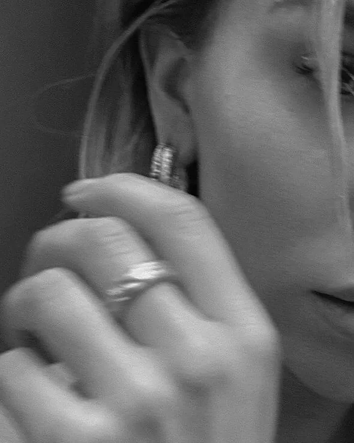 Photo en noir et blanc, plan rapproché d'une femme, main près de l'oreille, portant une bague et un bijou d'oreille brillant.