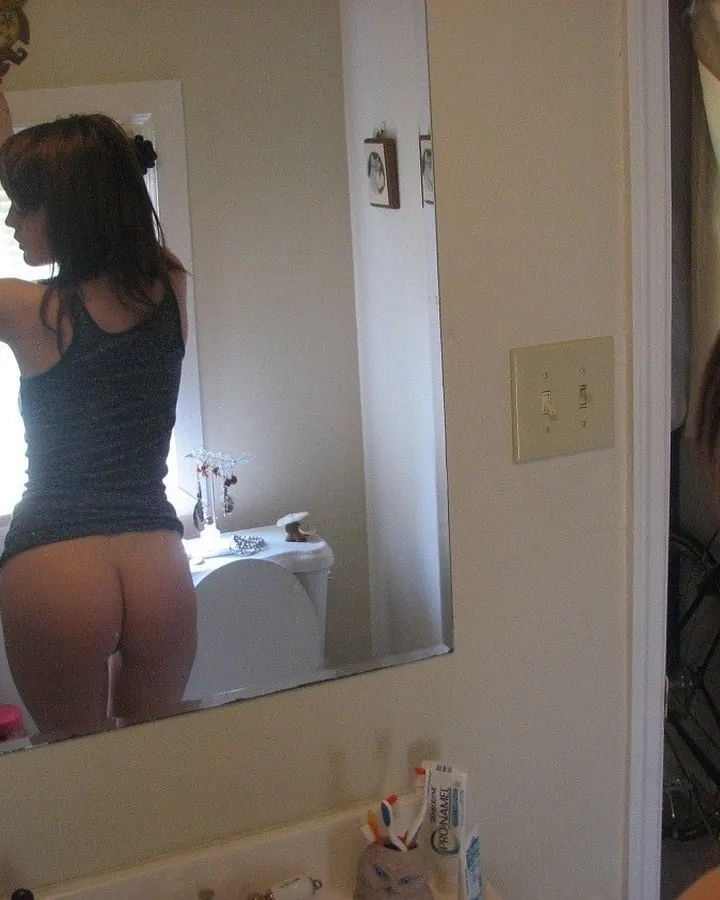 Femme en robe noire, tenant un appareil photo, reflet dans un miroir de salle de bain