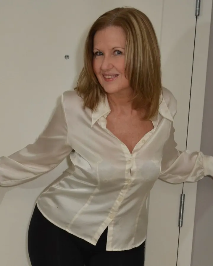 Femme en chemise satinée blanche, souriante, appuyée contre une porte