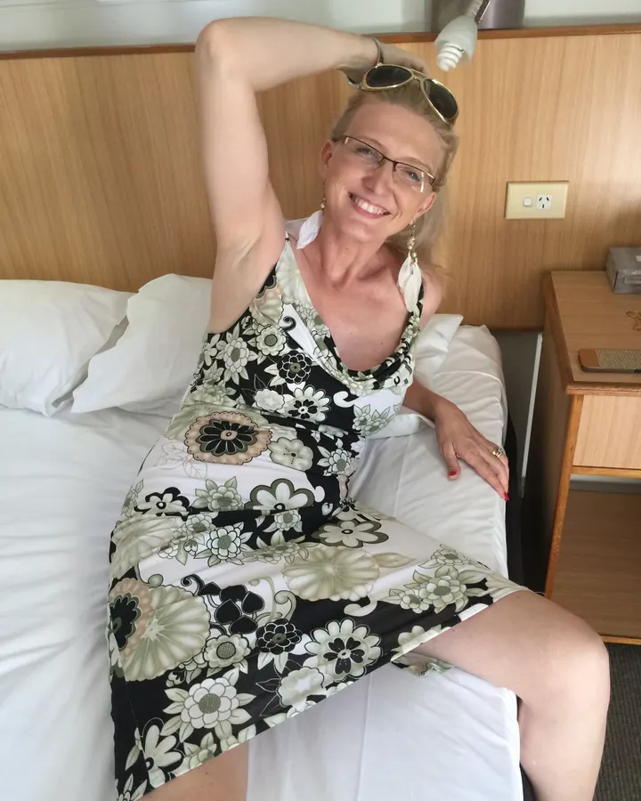 Femme souriante en robe fleurie, allongée sur un lit avec des lunettes de soleil sur la tête
