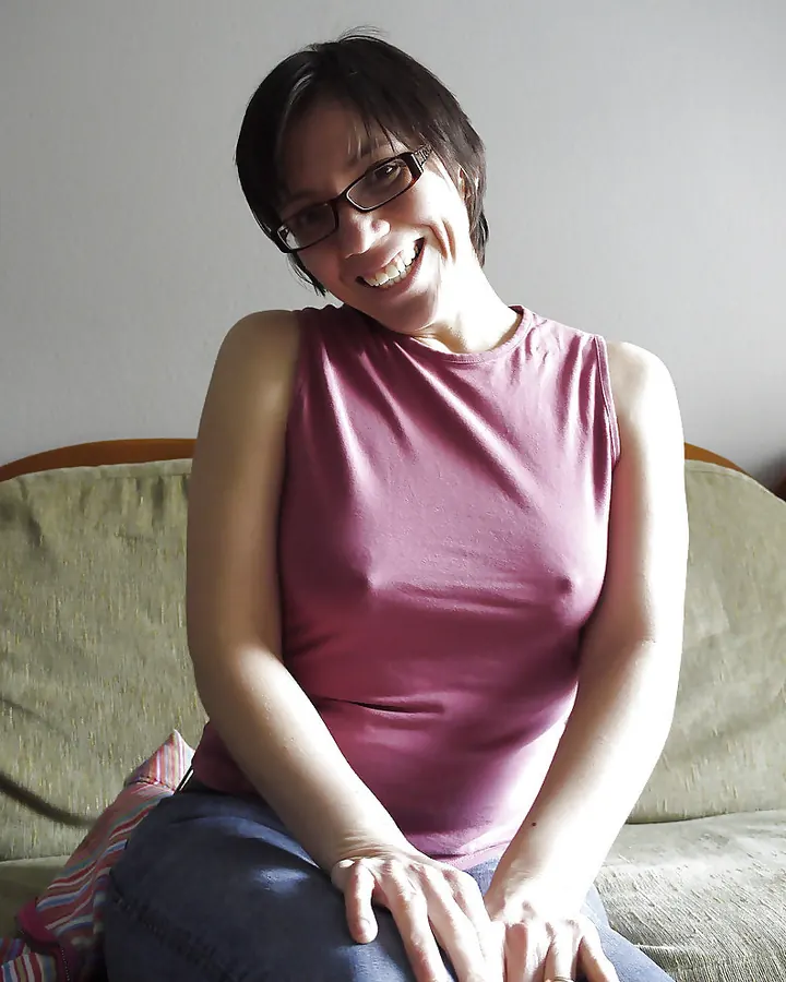 Femme aux cheveux bruns-noirs, vêtue d'un haut rose sans manches, souriant largement sur un canapé.