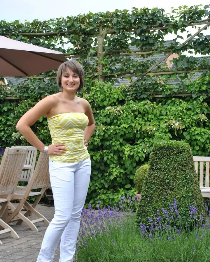 Femme aux cheveux châtains mi-longs portant un haut noir, assise, regardant l'appareil photo avec un sourire discret.