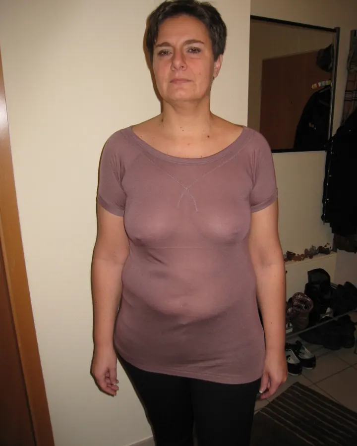 Femme en robe blanche, debout sur un rocher, regardant l'appareil, les mains sur les hanches.