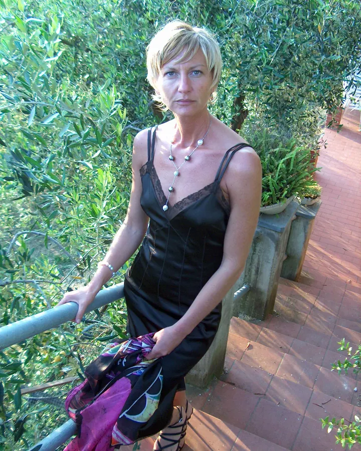 Femme blonde en haut noir, posant contre un mur blanc, regardant l'appareil photo