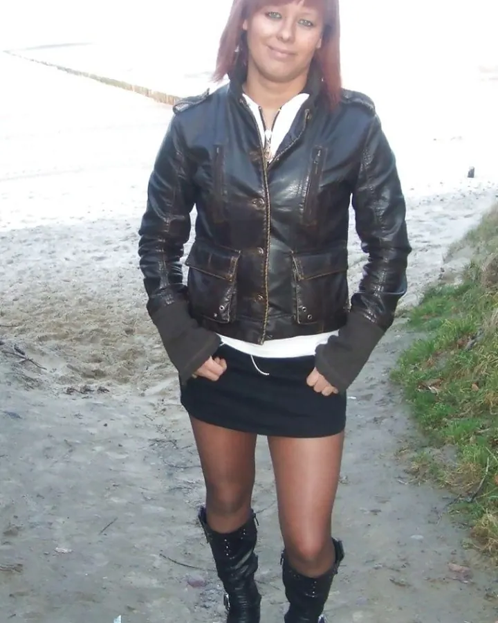Femme en veste en cuir noir, jupe courte, bottes, souriant sur une plage