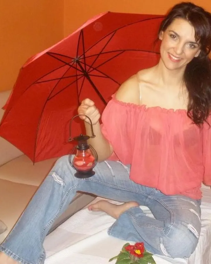 femme brune en blouse rose transparente et jean, parapluie rouge
