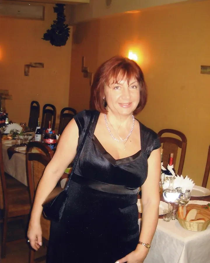 Femme aux cheveux roux portant une robe noire soyeuse, souriante, dans un restaurant élégant.