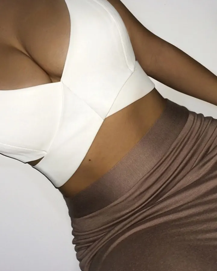 Plan rapproché d'une femme à la peau mate portant un haut blanc et une jupe marron, mettant en valeur sa poitrine.
