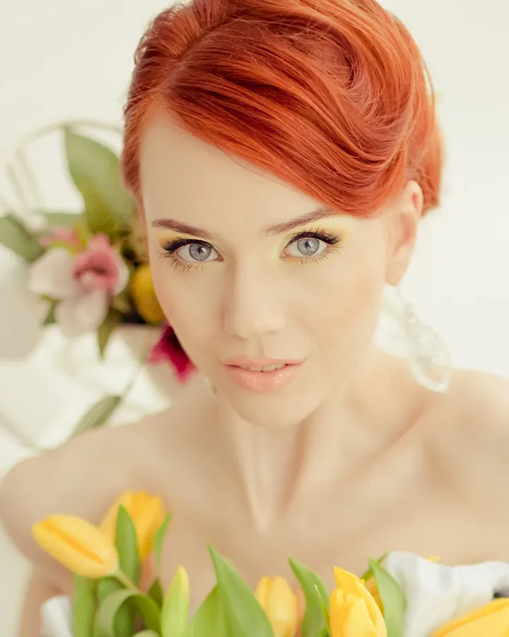 Femme aux cheveux roux, regardant l'appareil photo, entourée de tulipes jaunes.