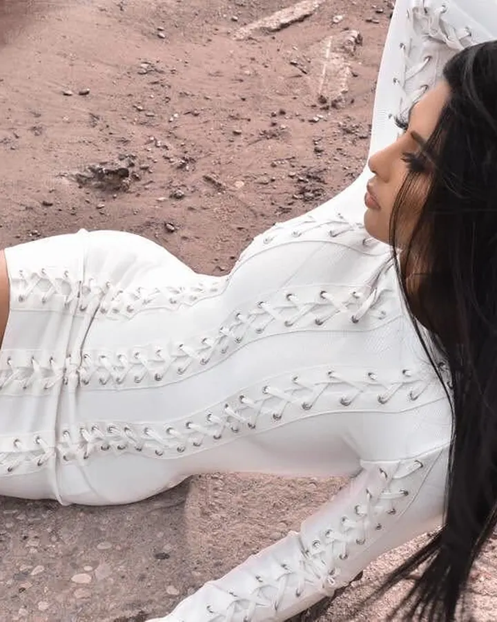 Femme aux cheveux noirs longs, vêtue d'une robe blanche à lacets, allongée sur un sol terreux, profil de côté, regard vers le haut.