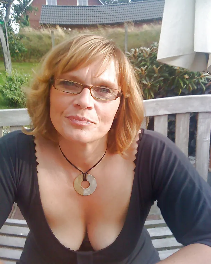 Femme aux cheveux blonds courts, portant des lunettes, vêtue d'un haut noir, assise sur une terrasse, regard direct.
