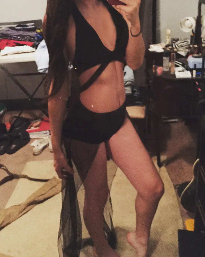 Jeune femme aux cheveux bruns-noirs, portant un body noir découpé, se tenant dans une chambre en train de prendre un selfie.