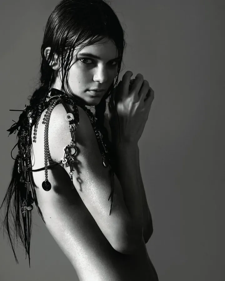 Femme en noir, en noir et blanc, avec des chaînes et des bijoux autour du cou, regardant la caméra avec un air intense.