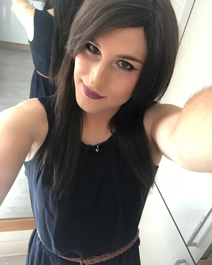 Femme aux cheveux foncés, regardant l'appareil photo, vêtue d'une robe bleue, dans une cuisine moderne.