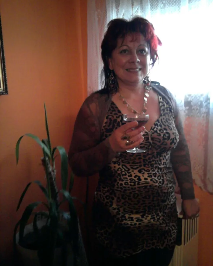 Femme aux cheveux roux portant un haut léopard, tenant un verre de vin dans une pièce aux murs orange.