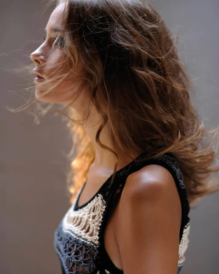Femme brune en haut tricoté noir et blanc, profil, cheveux au vent.
