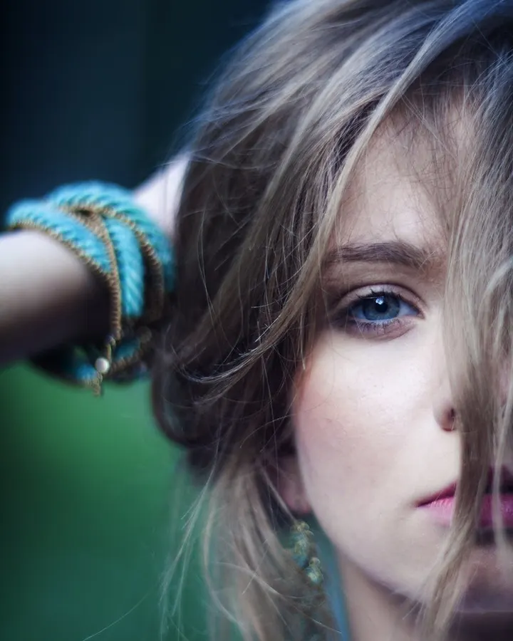 Portrait proche d’une jeune femme aux yeux bleus, cheveux blonds, portant un bracelet turquoise.