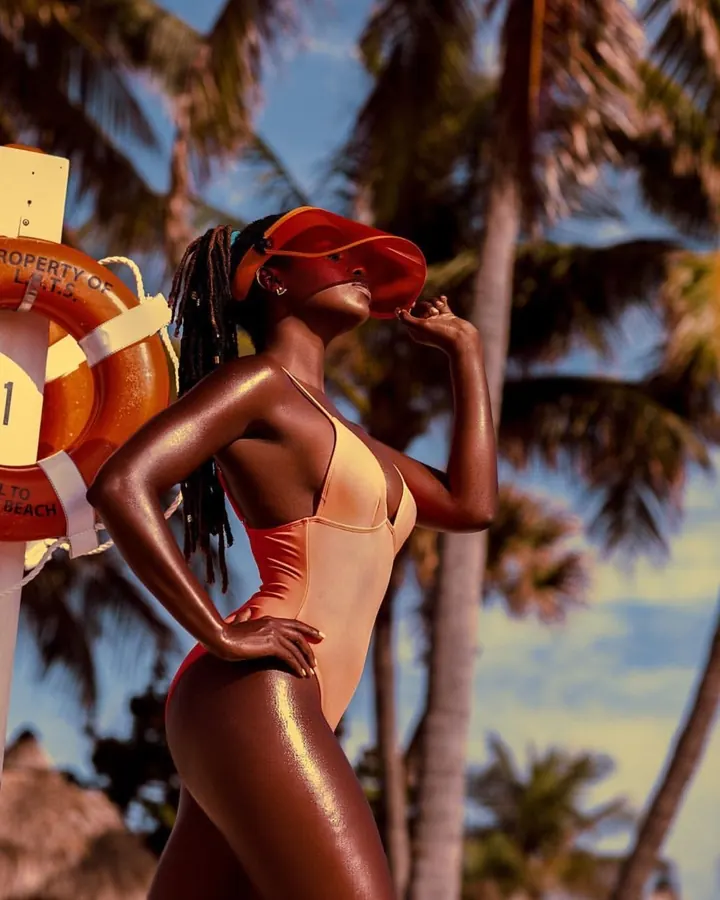 Femme aux cheveux noirs en maillot de bain orange, sur une plage, regardant vers le haut.