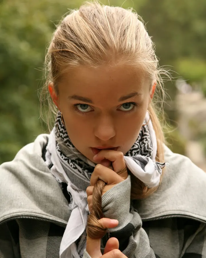 Femme aux cheveux blonds, portant un sweat gris et un foulard, regardant fixement l'appareil photo.