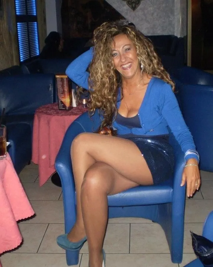 Femme aux cheveux blonds, portant un haut noir, assise sur un canapé, les pieds nus sur une table.