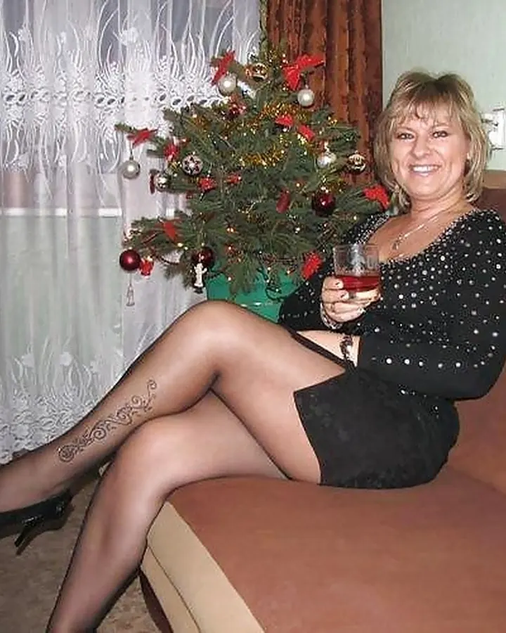 Femme européenne aux cheveux blonds, en robe blanche, posant dans une chambre, avec un miroir derrière elle.