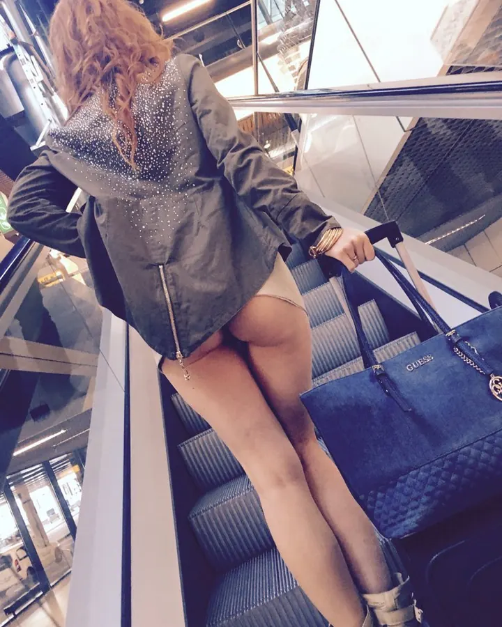 Femme vue de dos en veste militaire et collants, sur un escalator avec un sac Guess