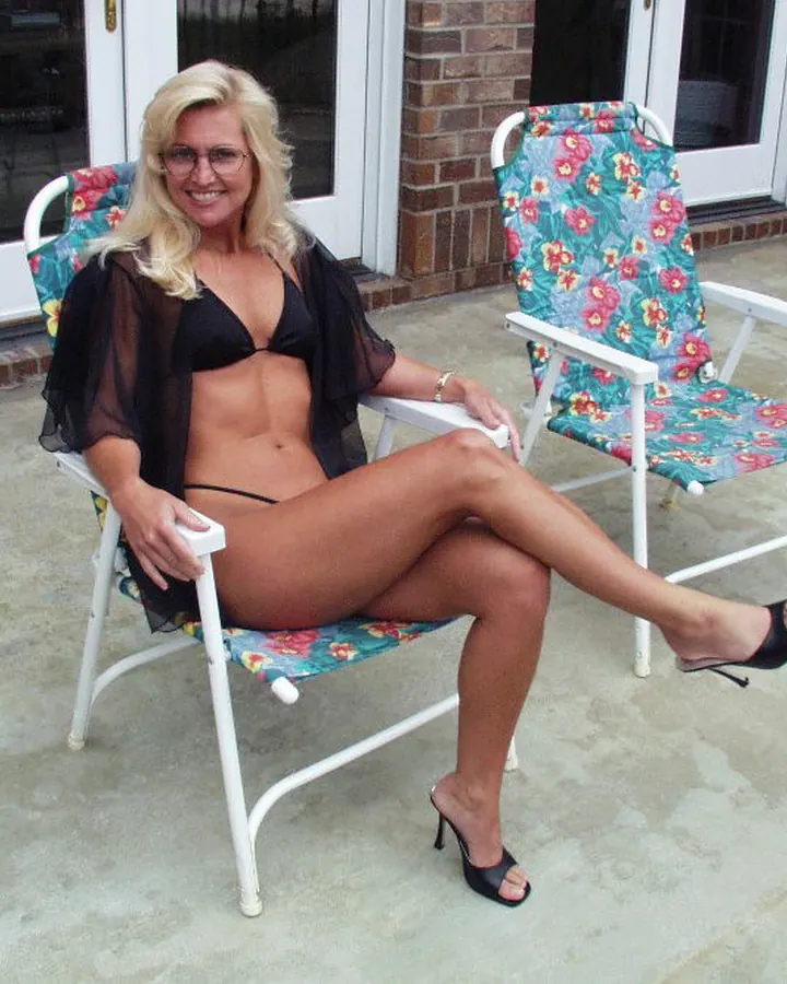 Femme blonde en bikini noir, assise dans une chaise longue fleurie