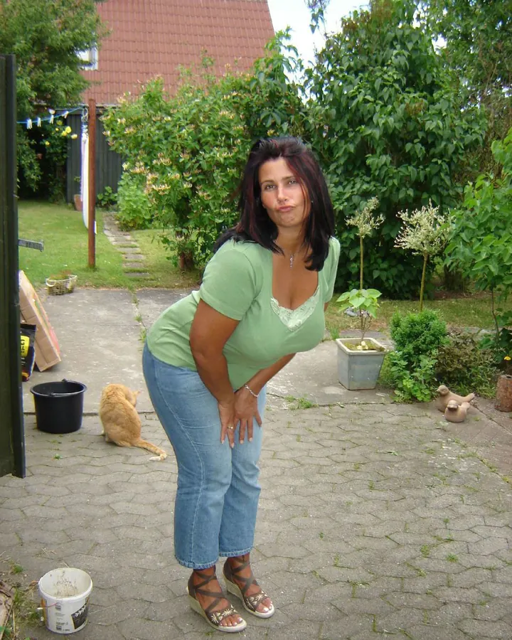 Femme brune en t-shirt vert et jean, mains sur les cuisses, dans un jardin