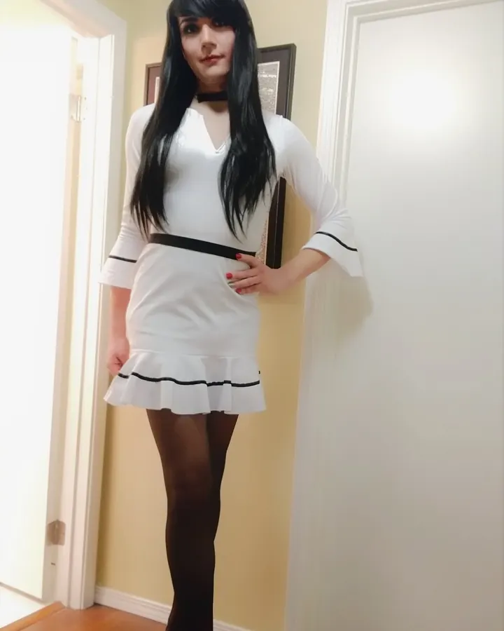 Jeune femme en robe blanche et collants noirs, posant dans un couloir