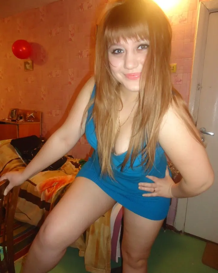 Jeune femme en robe bleue moulante, posant dans une chambre