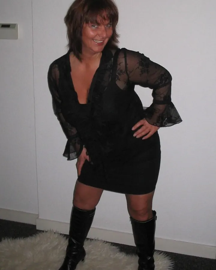 Femme aux cheveux bruns, en robe noire transparente, bottes noires, debout sur une fourrure blanche