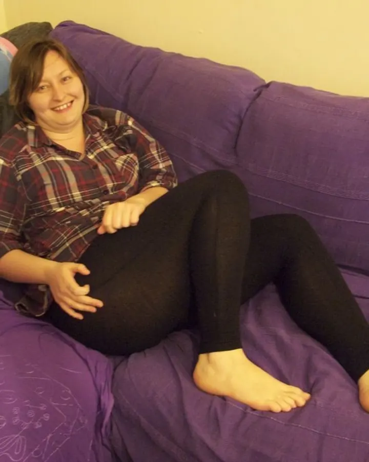 Femme aux cheveux châtains portant un haut noir, allongée sur un lit avec un regard direct