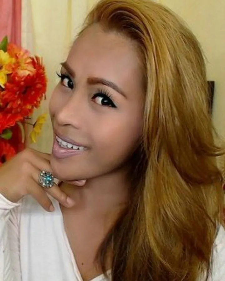 Femme aux cheveux roux, en haut rouge, souriant à l'appareil, fond flou.