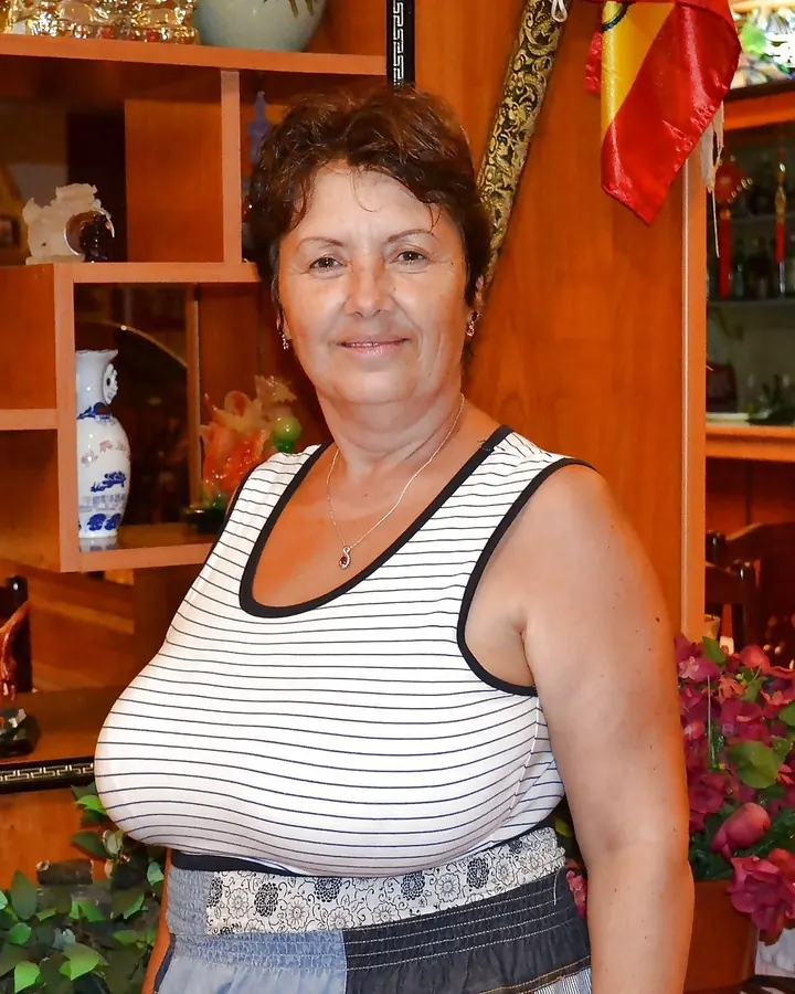 Femme blonde, souriante, en haut rayé, posant dans une pièce avec des objets décoratifs en bois et céramique.