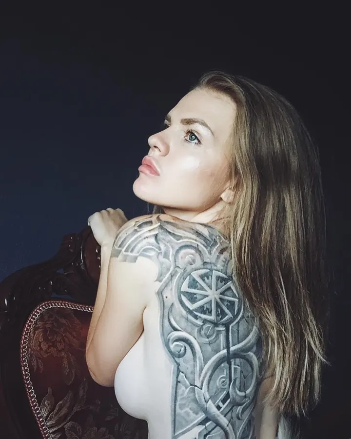Femme aux cheveux bruns, en haut noir, posant de profil avec les mains sur les hanches, sur fond blanc.