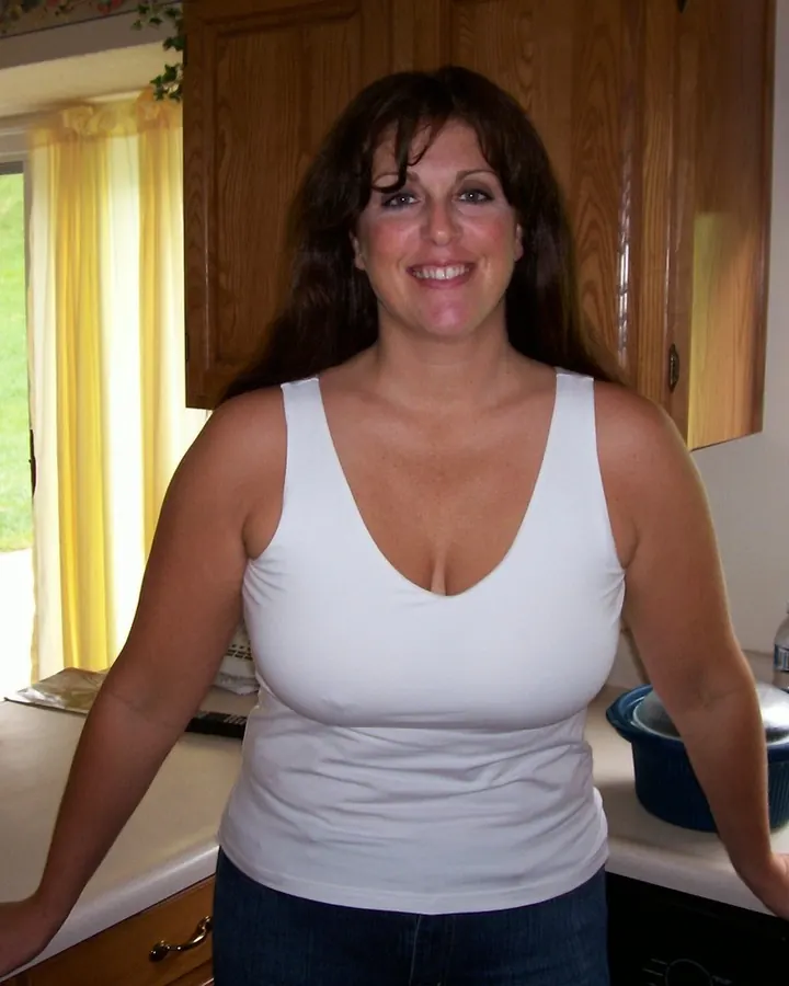Femme aux cheveux bruns, en haut noir, posant de profil avec les mains sur les hanches, sur fond blanc.