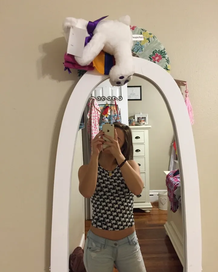 Jeune femme aux cheveux bruns, vêtue d'une tenue colorée, prenant un selfie en extérieur sur une pelouse.